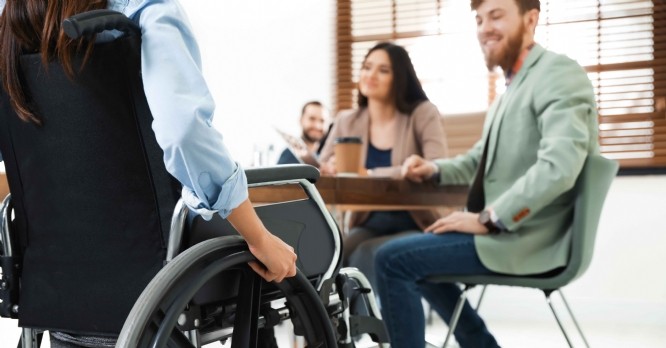 Young woman in wheelchair with colleagues at office, closeup
